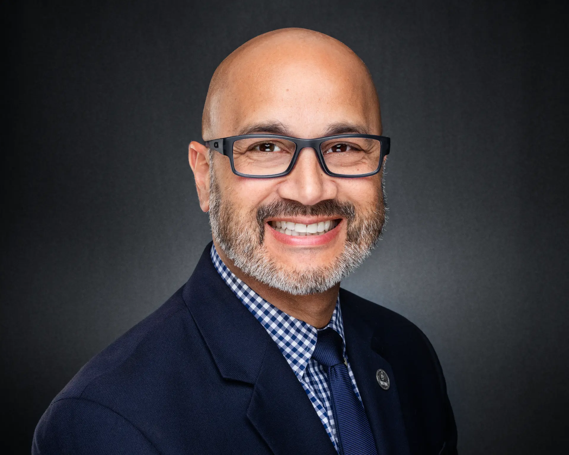 Studio headshot of a smiling professional man in a navy suit and tie