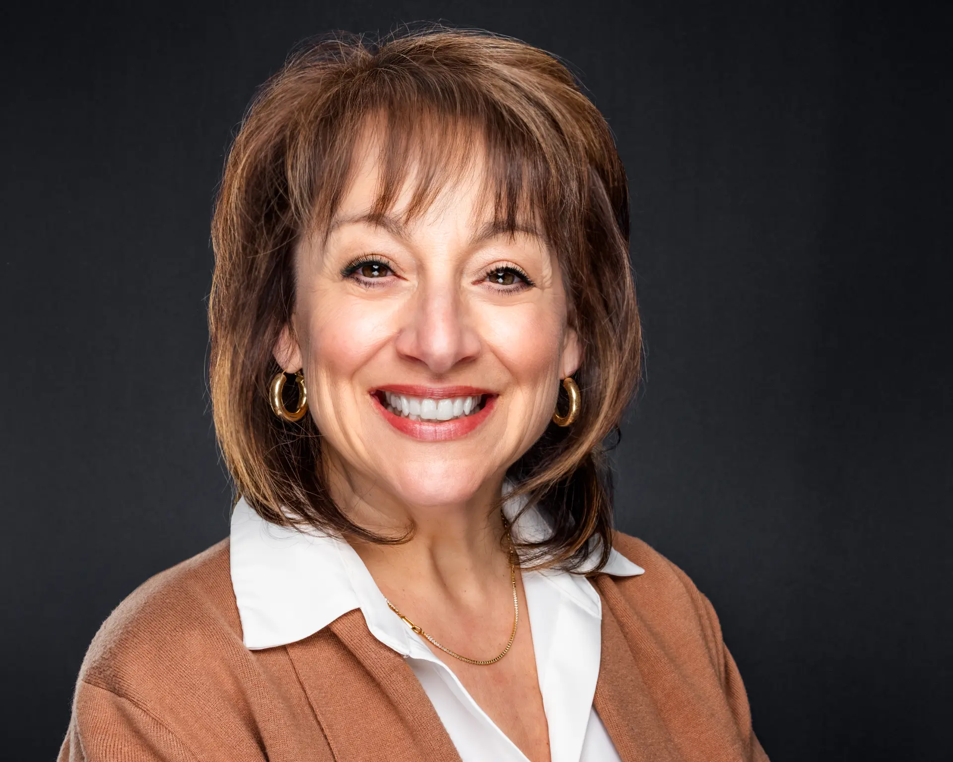 Studio headshot of a smiling professional woman in a camel cardigan