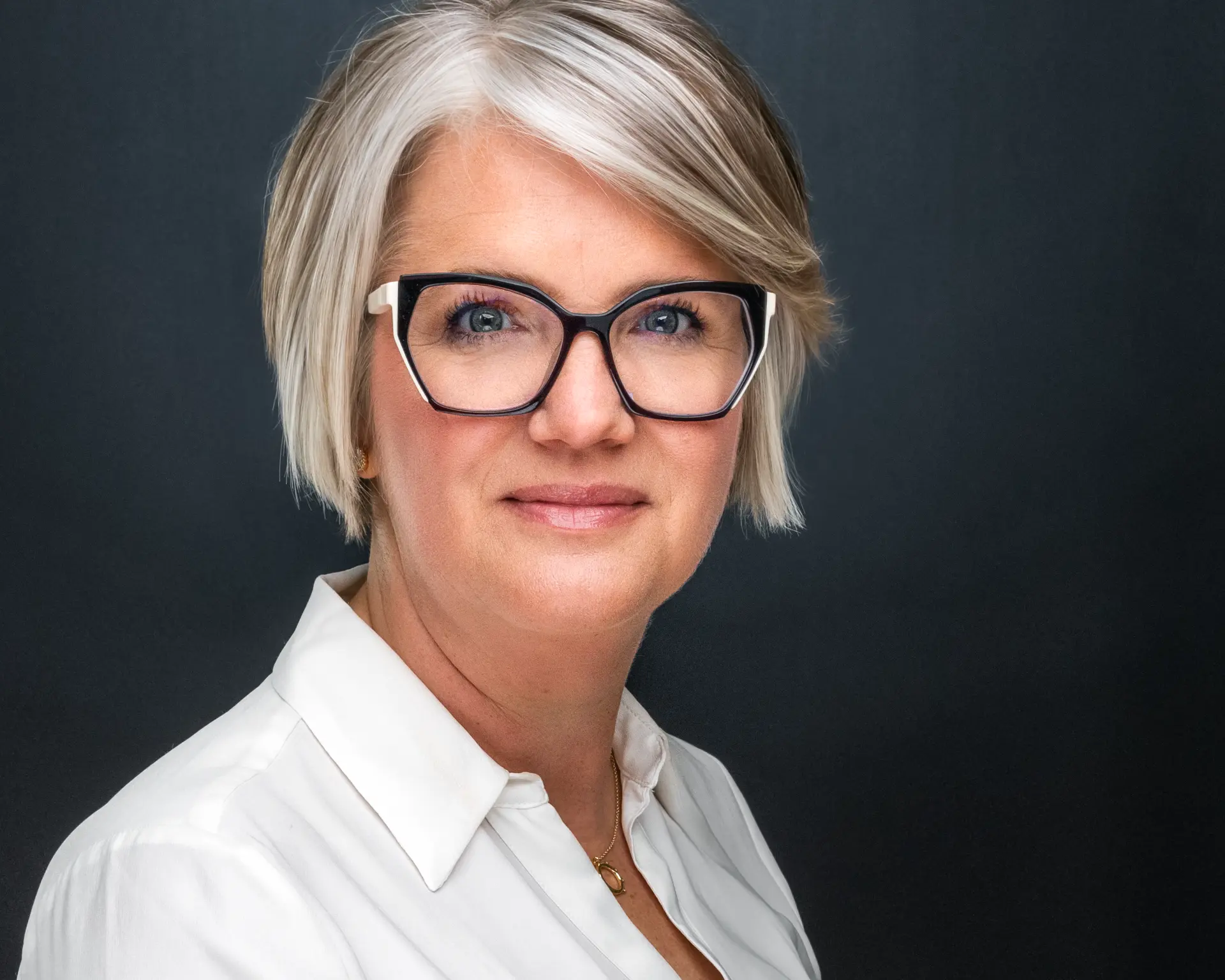 Studio headshot of a professional woman in a white shirt and statement glasses