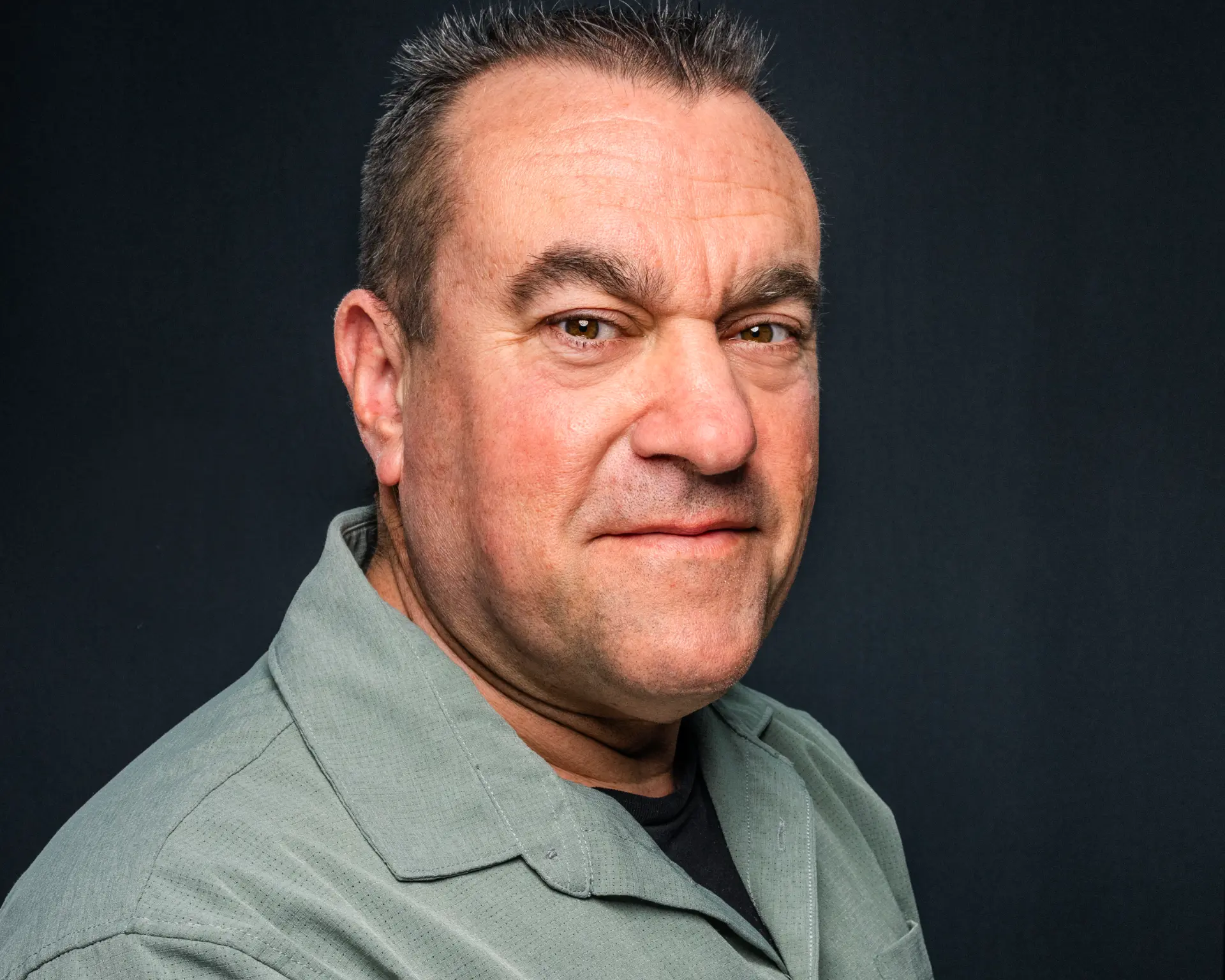 Studio headshot of a man in a sage green shirt against a dark background