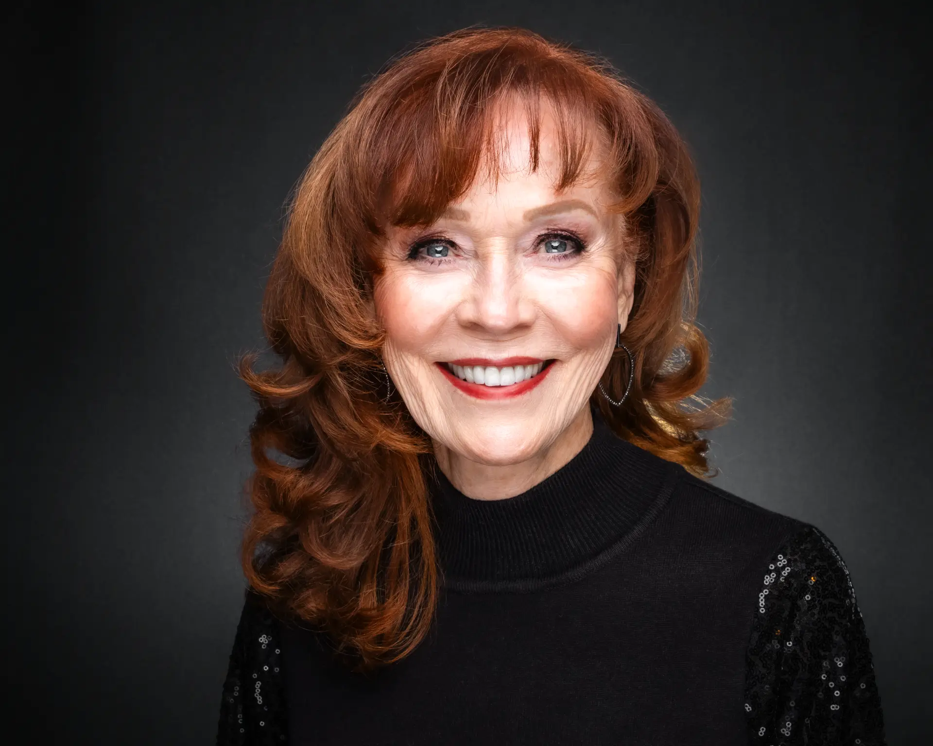Studio headshot of a smiling woman with auburn hair in a black turtleneck
